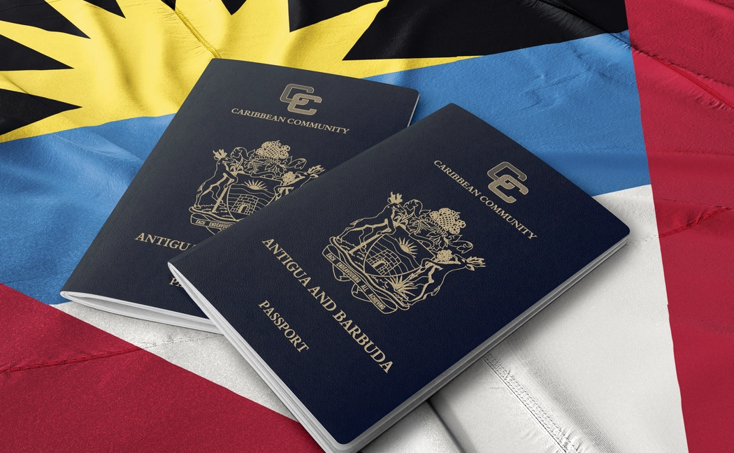Hai cuốn hộ chiếu Antigua and Barbuda màu xanh đen mạ vàng đặt trên nền lá cờ quốc kỳ